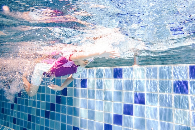 Bajo el agua niña linda está nadando en la piscina con su profesor de natación.