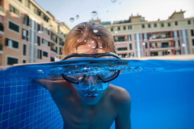 Bajo el agua de un niño con gafas de buceo respirando agua mientras nada en una piscina azul clara en el resort