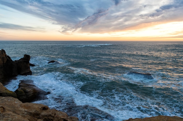 Agua ondulada de mar u océano con orilla pedregosa y cielo nublado al atardecer, belleza de la naturaleza.