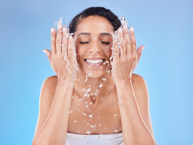 Água para cuidados com a pele e mulher lavando o rosto para um bem-estar limpo e saudável contra um fundo azul do estúdio limpeza de beleza e modelo feliz com esguicho para satisfação facial e rotina