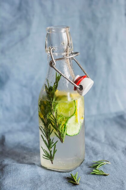 Agua de pepino, limón y romero en botellas sobre un fondo azul Bebida refrescante saludable