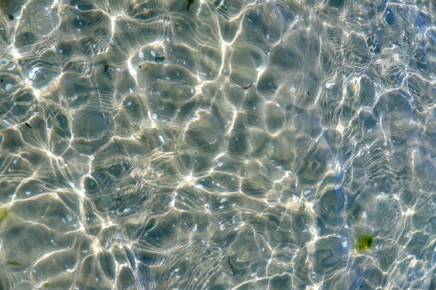 Agua de playa clara en un día de verano con espacio de copia Vista superior de las tranquilas olas del mar de marea baja durante la primavera Primer plano del reflejo del sol brillante que brilla en el océano poco profundo útil como fondo