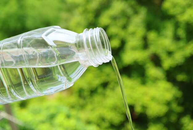 Agua potable de una botella de plástico con follaje verde en el telón de fondo