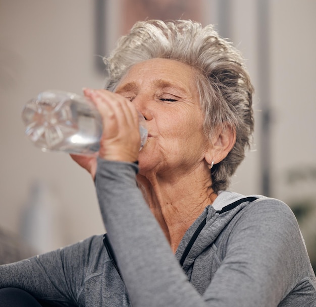 Agua potable fitness y jubilación con una mujer mayor en su casa para el bienestar o la hidratación Hacer ejercicio beber o sed con una mujer madura entrenando en su casa durante un entrenamiento para mantenerse activa