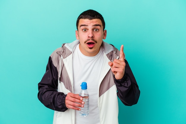 Agua potable del hombre caucásico deportivo joven aislado en azul que tiene una idea, concepto de la inspiración.