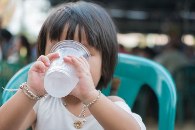 Agua potable de la muchacha del niño en el plástico de cristal.