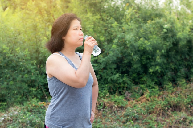 Agua potable de la mujer asiática después del ejercicio del deporte, mujer del deporte que sostiene la botella de agua pura