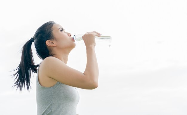 Agua potable de la mujer asiática joven de botellas plásticas después de correr. Chica sacia la sed después de fitn