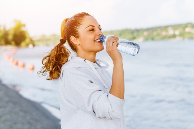 Foto agua potable de la mujer deportiva al aire libre en día asoleado.