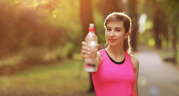 Agua potable de la mujer hermosa del corredor del atleta de la aptitud en el parque.