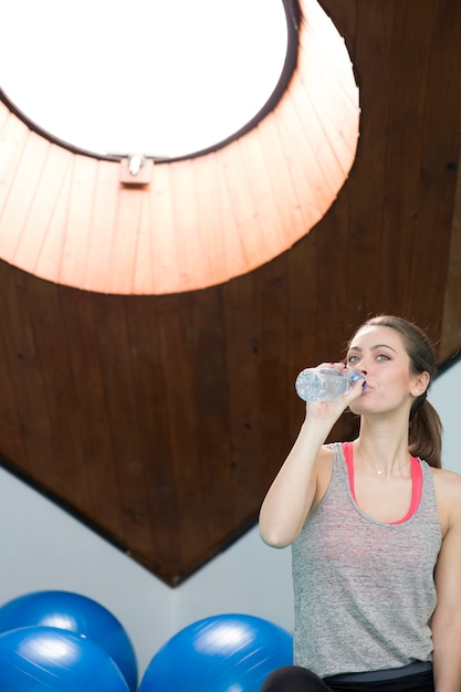 Agua potable de mujer joven de la botella en el gimnasio