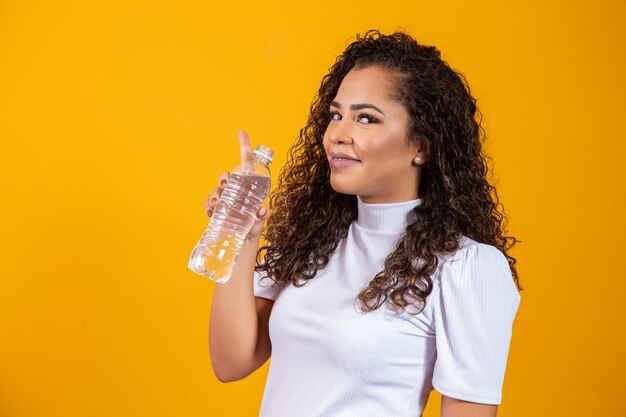 Agua potable de mujer joven sana sobre fondo amarillo con espacio para texto.