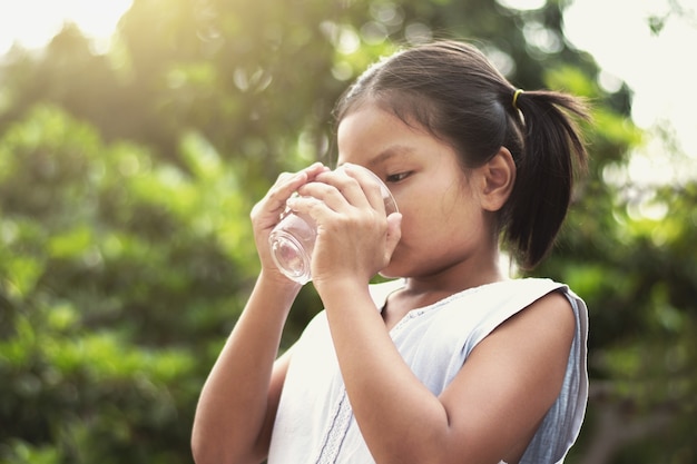 Agua potable niña asiática de vidrio con fondo de sol