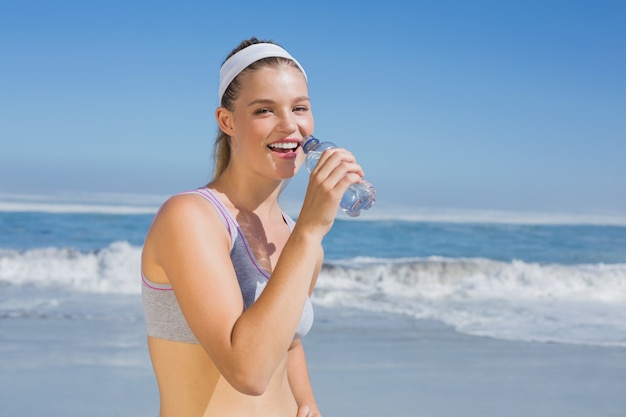 Agua potable rubia feliz deportiva en la playa