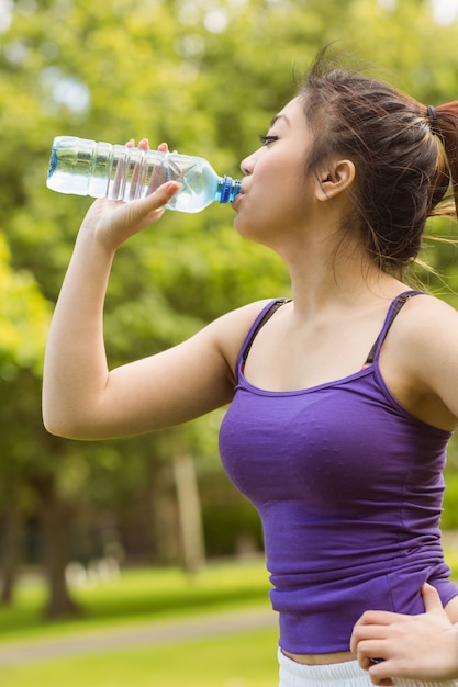 Agua potable sana y hermosa de la mujer joven en parque