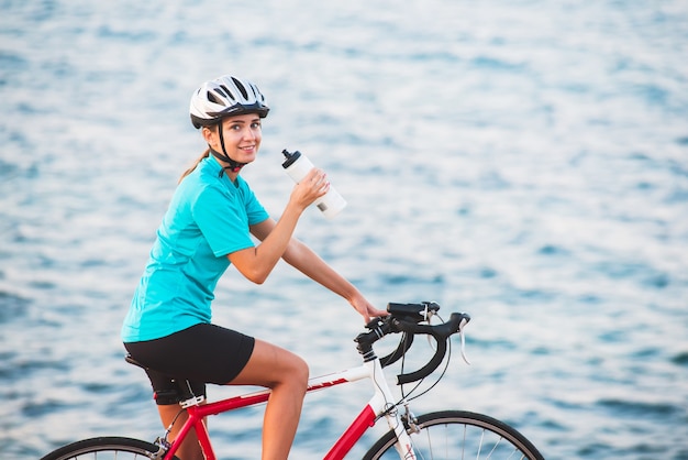 Água potável de ciclista feminina com mar