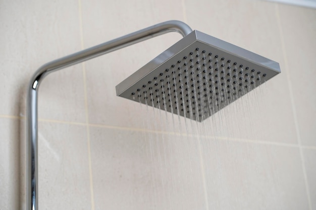 Agua que sale del cabezal de la ducha en el baño con fondo de azulejos beige Diseño de interiores hogareño simple, elegante y moderno
