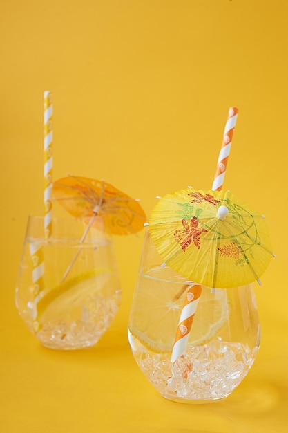 Água refrescante com limão e gelocom tubos decorativos e guarda-chuvas  tubos de papel amarelo e laranja matar a sede