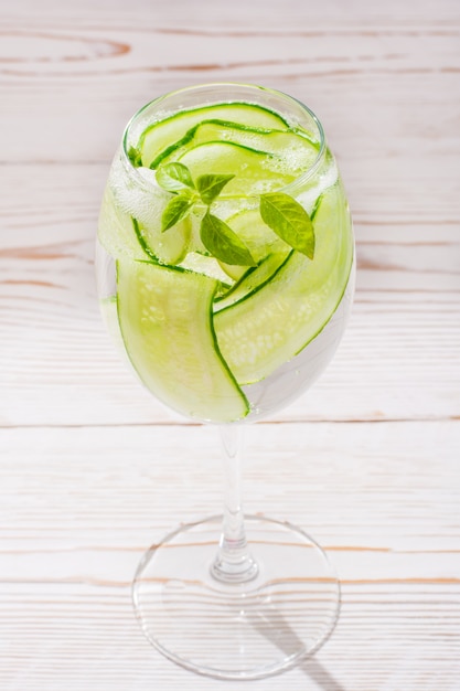 Agua refrescante con rodajas de pepino y hojas de albahaca en un vaso sobre una mesa de madera