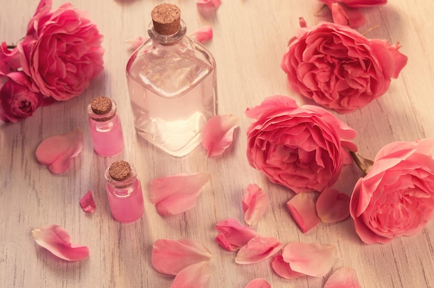 Agua de rosas y aceite en botellas de vidrio con flores y pétalos de rosas frescas sobre fondo de madera Concepto de SPA y aromaterapia