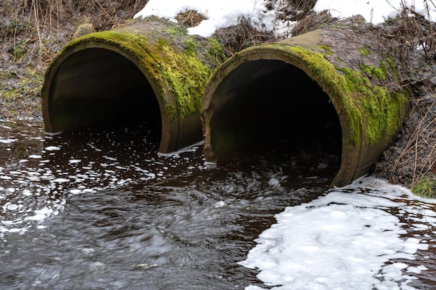 Agua sucia con fugas de grandes tuberías de hormigón La nieve se encuentra en las tuberías Aguas residuales sucias de la tubería contaminación ambiental Problema ambiental