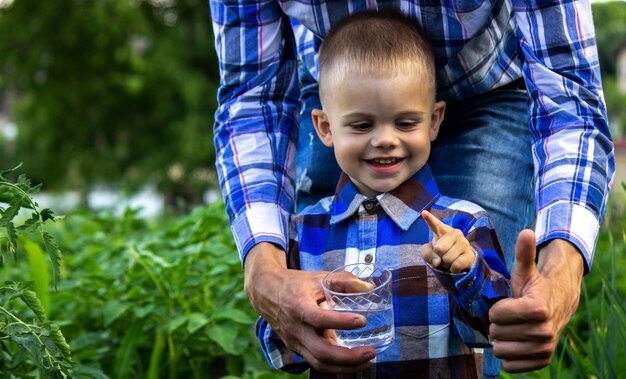 Agua en un vaso en manos de un niño y un padre. Naturaleza.