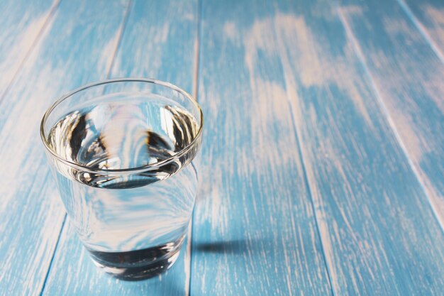 Agua en vidrio sobre fondo azul y mesa de madera.