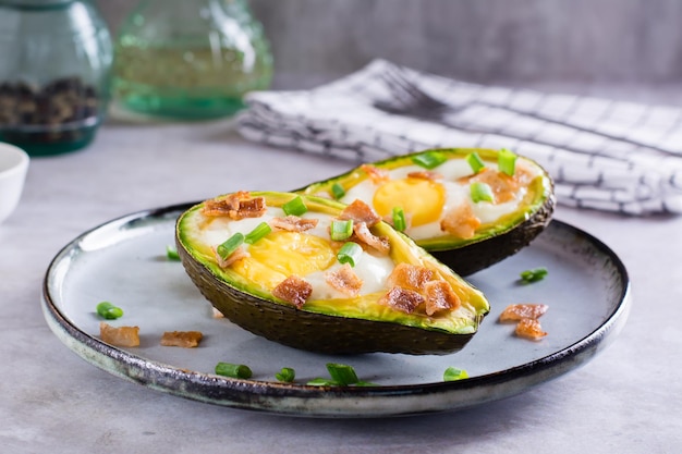 Aguacate al horno con tocino de huevo y cebollino en un plato sobre la mesa para una dieta cetogénica