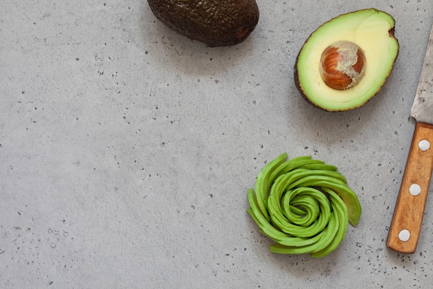 Foto aguacate cortado a la mitad y rosa sobre fondo de hormigón