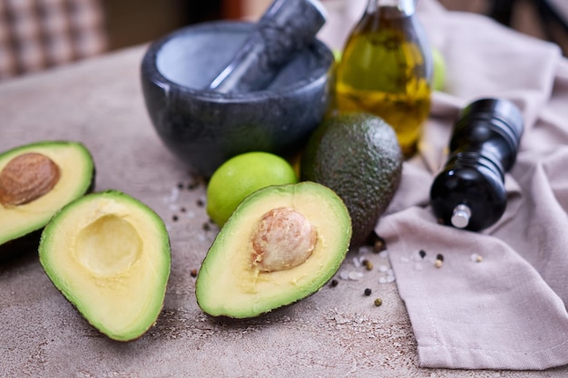 Aguacate fresco cortado por la mitad y mortero de mármol sobre mesa de hormigón gris