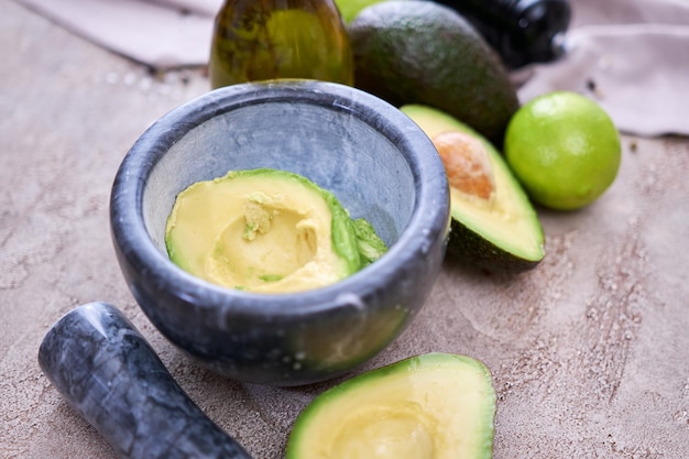 Aguacate fresco cortado por la mitad y mortero de mármol sobre mesa de hormigón gris