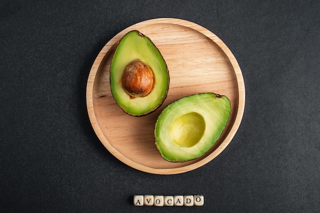 Foto aguacate fresco se encuentra en placa de madera sobre fondo negro letras de aguacate en cubos de madera