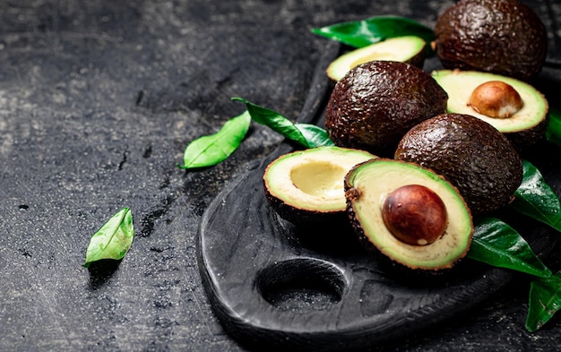 Aguacate fresco con follaje sobre una tabla para cortar