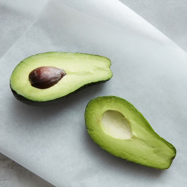 Aguacate de fruta representada en papel de hornear blanco sobre la mesa. Aguacate de color verde con hueso marrón.