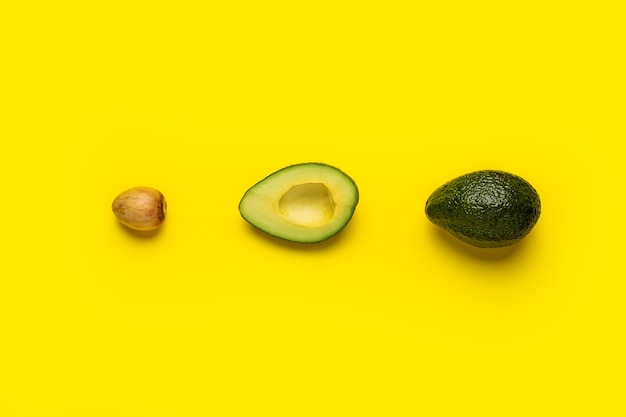 Aguacate con hueso, medio y entero sobre un amarillo brillante