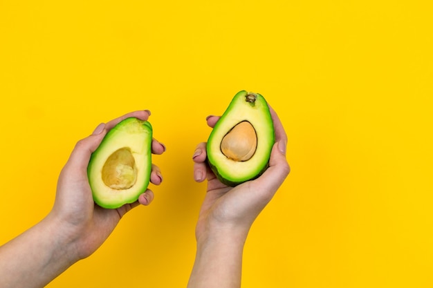 El aguacate en una mano femenina está aislado en un amarillo