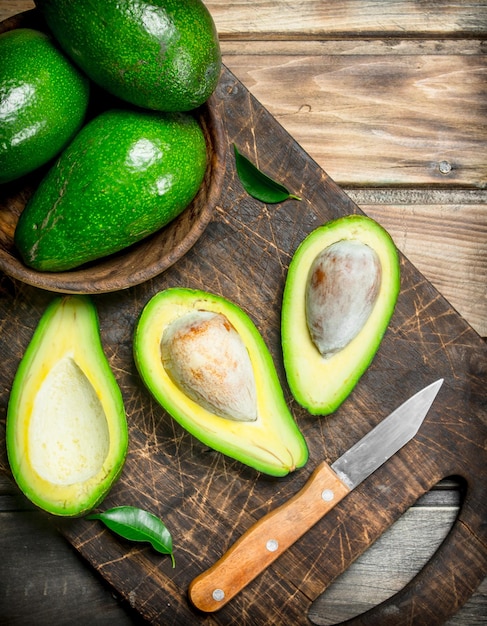 Aguacate en un recipiente sobre una tabla de cortar negra con un cuchillo