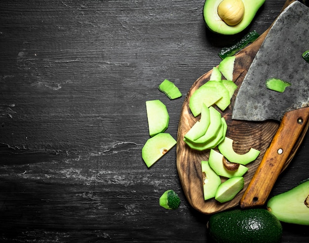 Aguacate en rodajas con un hacha en el tablero. Sobre un fondo de madera negra. Vista superior.