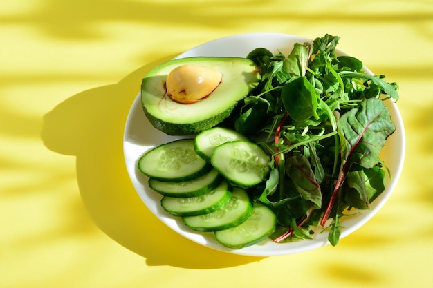 aguacate con rodajas de pepino y verduras de ensalada en el plato aislado con rayos de sol