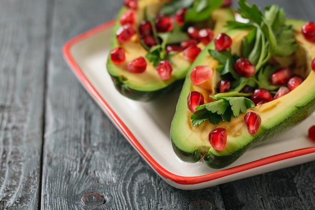 Aguacate con semillas de granada, salsa balsámica, limón y hierbas en el tazón blanco y rojo.