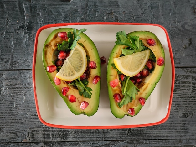 Aguacate con semillas de granada, salsa balsámica y limón sobre la mesa de color negro oscuro. Cocina vegetariana para adelgazar. La vista desde la cima.