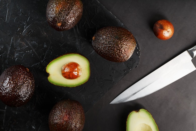 Aguacates maduros en una canasta sobre una mesa negra, con una fruta cortada y un hueso