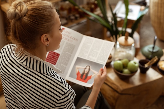 Aguardando procedimento. Visitante loira concentrada se divertindo com revistas de beleza e artigos úteis