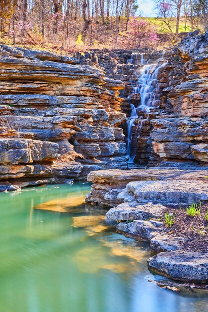 Foto Águas azul-petróleo mostram rochas ao lado de penhascos irregulares com cachoeira