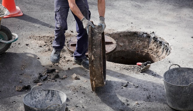 aguas residuales y alcantarillas en manos de trabajadores uniformados y asfaltados en el lugar de construcción