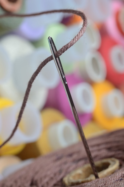 Una aguja de coser con hilo marrón a través del ojo de la aguja. macro.