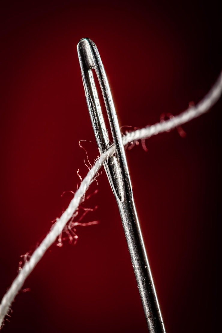 Foto aguja con hilo sobre un fondo rojo.