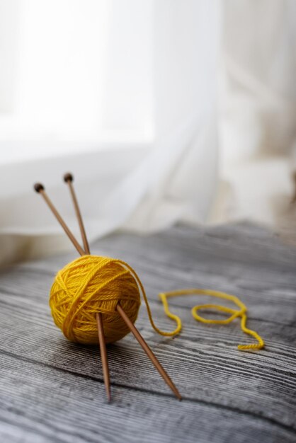 Agujas de tejer de bola de lana de color amarillo sobre el fondo de madera