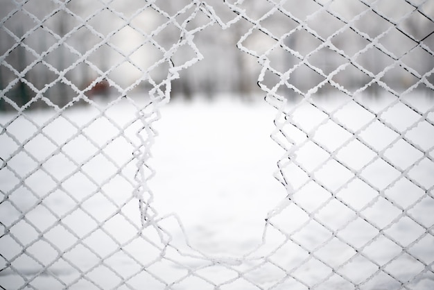 Agujero en la malla de acero en invierno. Nieve y hielo.