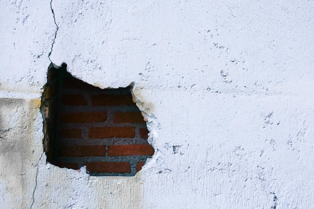 Agujero en la pared rota y ladrillos viejos sobre fondo blanco Gran grieta en la pared de una vieja casa de ladrillos yeso desmoronado y ladrillos rotos agrietados